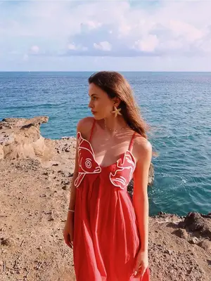 Woman standing by sea wearing red fish dress and starfish earrings