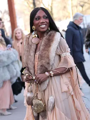 Doechii wearing a flowy dress with fur accessories and a gold seashell bag
