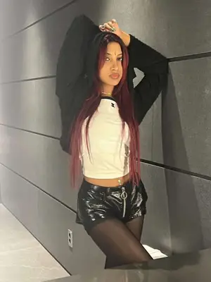 Person posing while wearing a black jacket, white shirt, leather pants, and tights