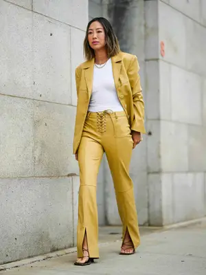 Woman wearing yellow leather blazer and pants, white fitted tee, black multi-strap square-toe heels, and classic gold jewelry