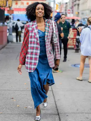 Woman wearing a mixed-print plaid blazer, denim dress, silver Tabi shoes, and hoop earrings