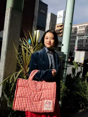 Woman carrying red gingham nylon tote bag while wearing blazer and button-down top
