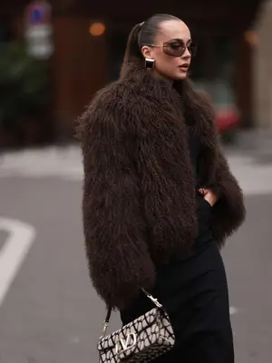 Woman wearing brown fluffy coat, Valentino bag, and oversized brown Miu Miu sunglasses