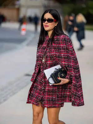 Woman wearing tweed cape coat, black handbag, and sunglasses