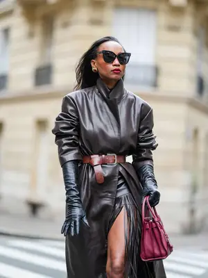 Woman wearing leather coat and fringe mini skirt, gloves, and red handbag