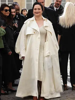 Lily Gladstone wears an ivory coat and light beige dress