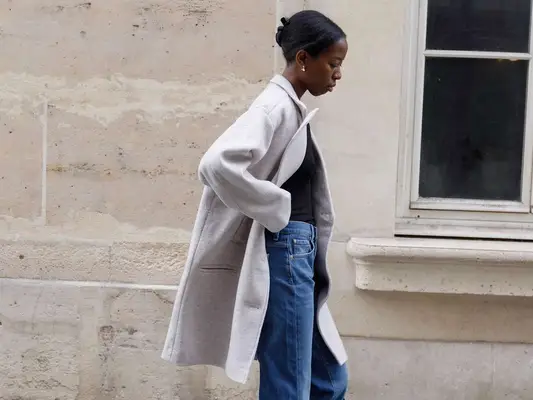 Sylvie Mus wears a gray coat, black bodysuit, and jeans