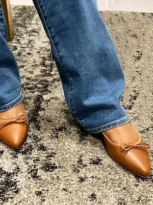Close-up of person wearing tan pointed-toe flats and jeans
