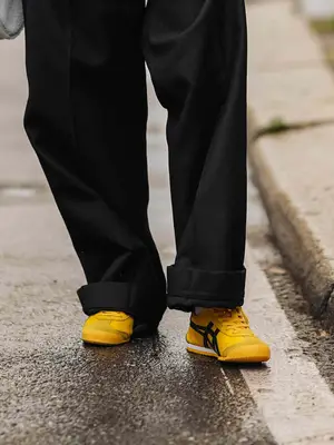 Close-up of person wearing yellow Onitsuka Tiger sneakers and black pants