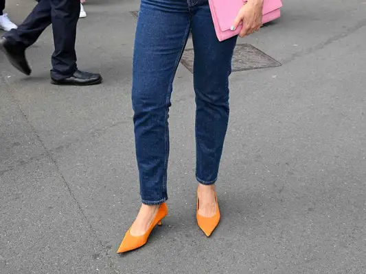 Close-up of woman wearing dark wash jeans, pink handbag, and orange kitten heels