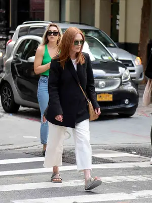 Julianne Moore wears a black blazer, white jeans, gray Birkenstocks, aviator sunglasses, and a tan crossbody bag