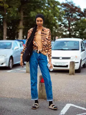 Model Ugbad Abdi wears a black headscarf, tiger print shirt, blue jeans, black socks, and brown Birkenstock sandals after the Simone Rocha show during London Fashion Week