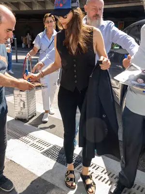 Actress Marion Cotillard wears black Birkenstocks, black skinny jeans, a black vest, and a blue and red ball cap