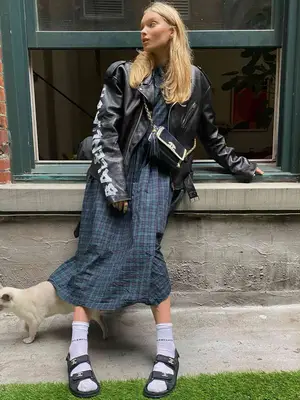 Elsa Hosk wearing white socks with black Birkenstocks, a blue plaid midi dress, and a black leather jacket