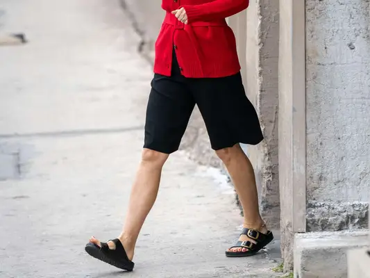 Close-up of Gwyneth Paltrow wearing a red sweater, black Bermuda shorts, and black Birkenstocks