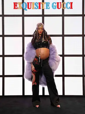 Rihanna wears a black crop top, jeans with dragon embroidery, and purple fur coat to the Gucci Fall 2022 show
