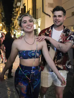 Haley Lu Richardson wears a blue printed tube top, matching pants, and a clutch with a beaded chain