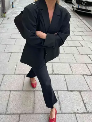 Matilda Djerf wears an oversized black suit, black shoulder bag, and red ballet flats