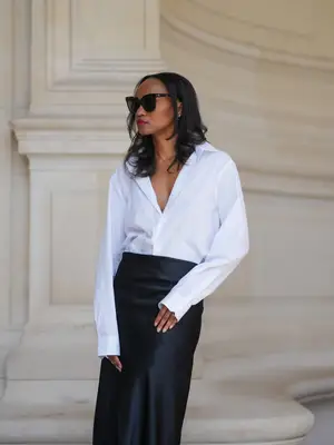 Emilie Joseph wears a white button-down shirt, black maxi skirt, and sunglasses