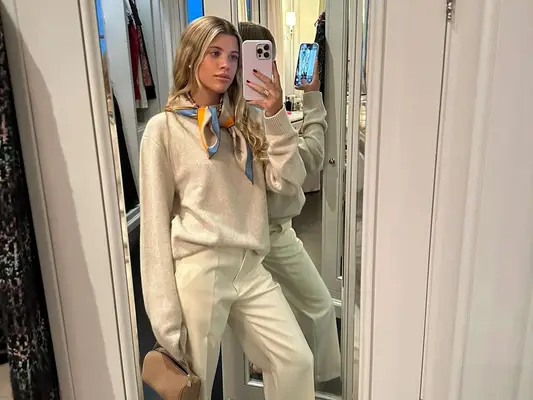 Sofia Richie Grainge wears a heathered sweater, white trousers, tan handbag, and patterned silk scarf