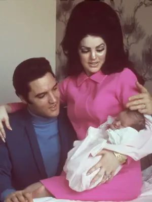 Priscilla Presley wears a hot pink shift dress and beehive hairstyle while cradling daughter Lisa Marie with Elvis
