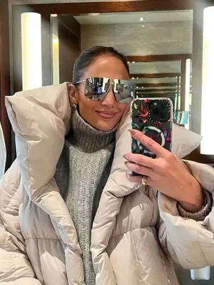 Jennifer Lopez wearing a white puffer coat, gray turtleneck and silver sunglasses.