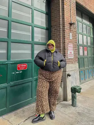 Imani Randolph wears a black puffer jacket, green cargo pants, heathered shoulder bag, and sunglasses