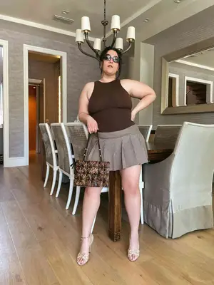 Nadia Aboulhosn wears a brown bodysuit, plaid pleated mini skirt, neutral strappy heels, and brown and black handbag