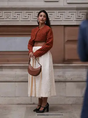 Bettina Looney wears a patterned cropped jacket, beige midi skirt, brown Prada bag, and silver earrings