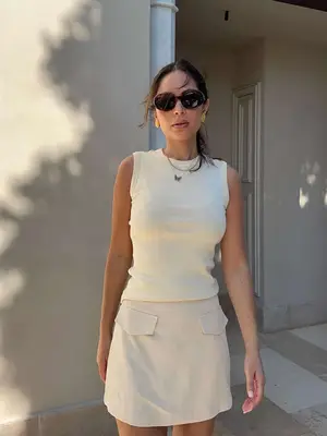 Marianna Hewitt wears a white tank, pocketed mini skirt, tortoise oval sunglasses, and simple gold jewelry