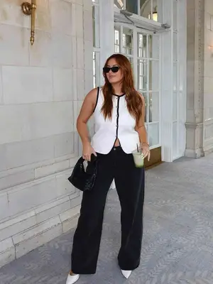 Woman wearing white vest top with black trim, black wide leg trousers, black woven bag, and sunglasses