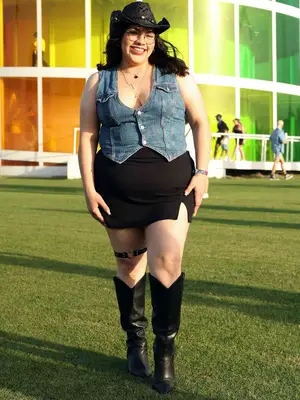 Woman wearing denim vest top, black mini skirt, cowboy boots and hat