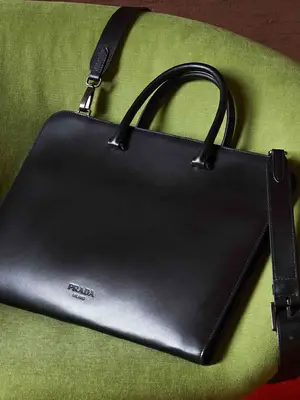 Black Prada briefcase-style handbag with top handles and crossbody strap on green chair