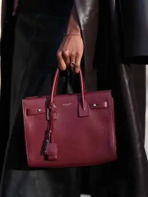 Close-up of woman holding cherry red Saint Laurent Sac de Jour bag and wearing leather trench coat