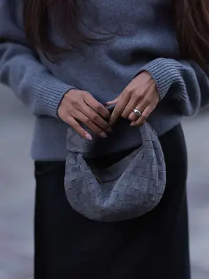Close-up of woman wearing sweater and black skirt and carrying gray woven Bottega Veneta Jodie bag