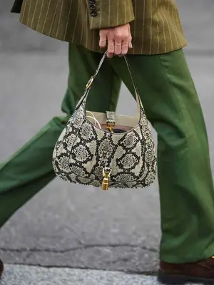 Close-up of woman wearing pinstriped blazer and green pants and carrying snakeskin Gucci bag