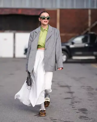 Woman wearing leopard print sneakers, gray blazer, green cropped button-down, white maxi skirt, green sunglasses, and handbag