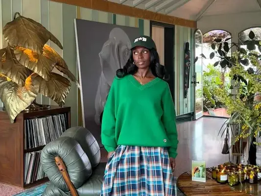 Toni Bravo wears a green sweater, tartan skirt, and baseball cap