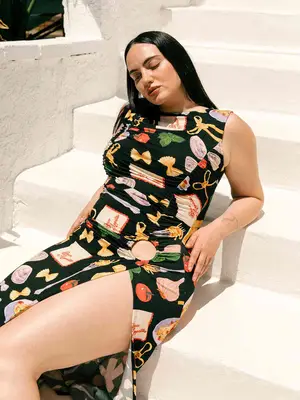 Woman wearing a pasta-printed black sleeveless midi dress with a high slit and cutout hip detail