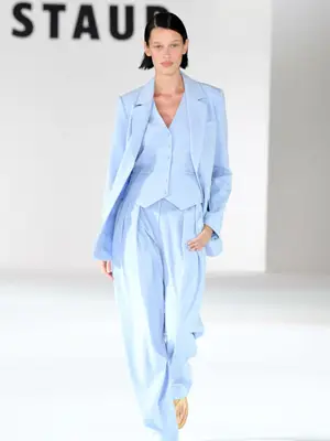 Model on the Staud runway wearing a periwinkle suit comprising a vest, jacket, and wide leg trousers