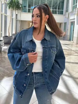 Ashley Graham wearing a mid-wash denim jacket, jeans, white tank top and earrings. 