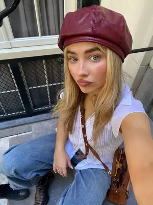 Sabrina Carpenter wearing a white shirt, mid-wash denim, and a red leather hat
