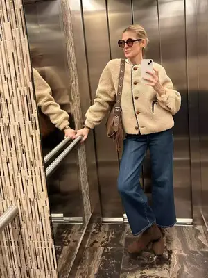 Kelly Rutherford posing for a photo while wearing jeans, a cream jacket, and suede boots