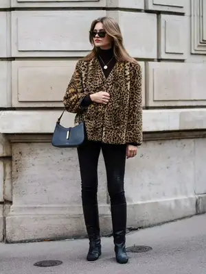 Person wearing a cheetah print coat, turtleneck, black skinny jeans, and tall boots