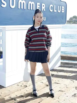 Bella Poarch wears a striped long-sleeve polo top, pleated navy mini skirt, gray knee-high socks, and pointed Mary Janes