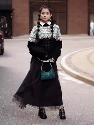 Woman wears long black tulle skirt, patterned sweater, pinstriped button-down, green Guess bag, and black platform loafers