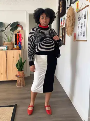 Alexis Page wears a black and white striped sweater, black and white color block midi skirt, and scarlet red Mary Jane shoes