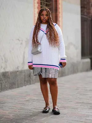 Woman wearing cable knit sweater with colorful striped trim, sparkly skirt, silver Telfar bag, and black Mary Jane shoes