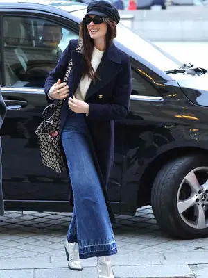 Anne Hathaway wearing jeans with a navy wool coat and silver boots