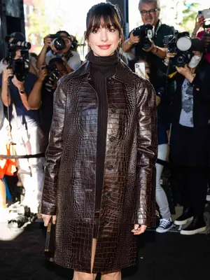 Anne Hathaway wearing a Michael Kors brown croc-effect coat, chocolate brown turtleneck, and wispy bangs hairstyle